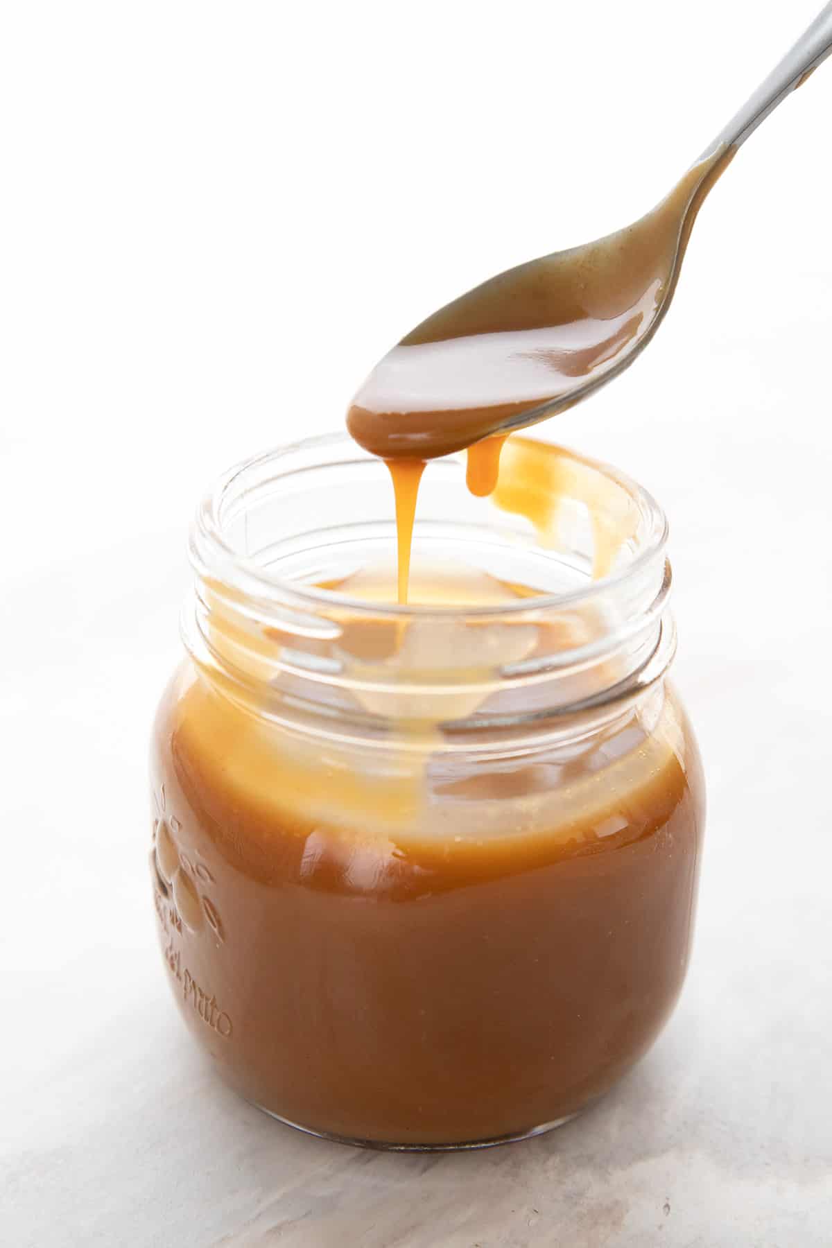 A spoon drizzling keto dulce de leche into a glass jar.