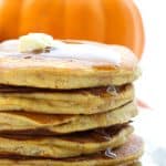 Close up shot of a stack of Keto Pumpkin Pancakes with syrup dripping down, in front of a small pumpkin.