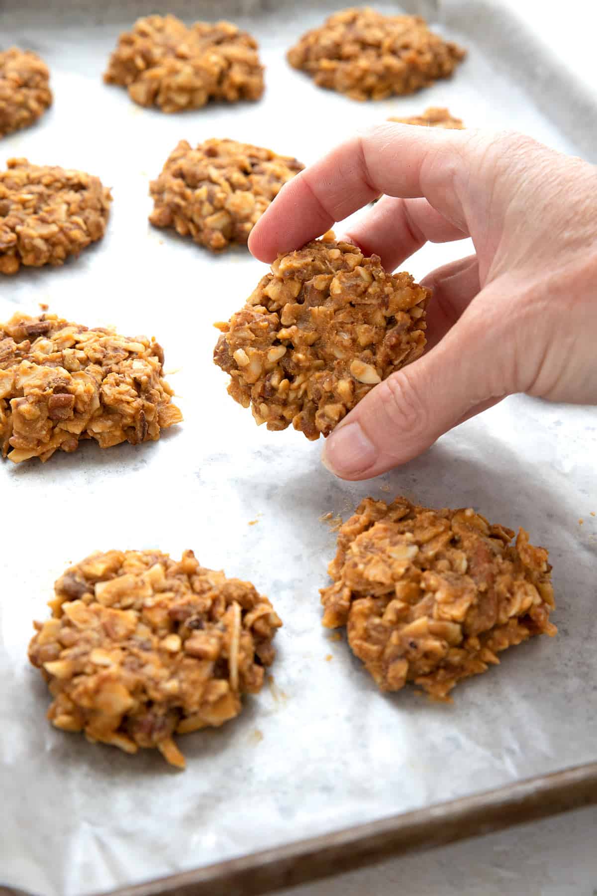 A hand lifting a keto no bake cookie from a cookie tray.