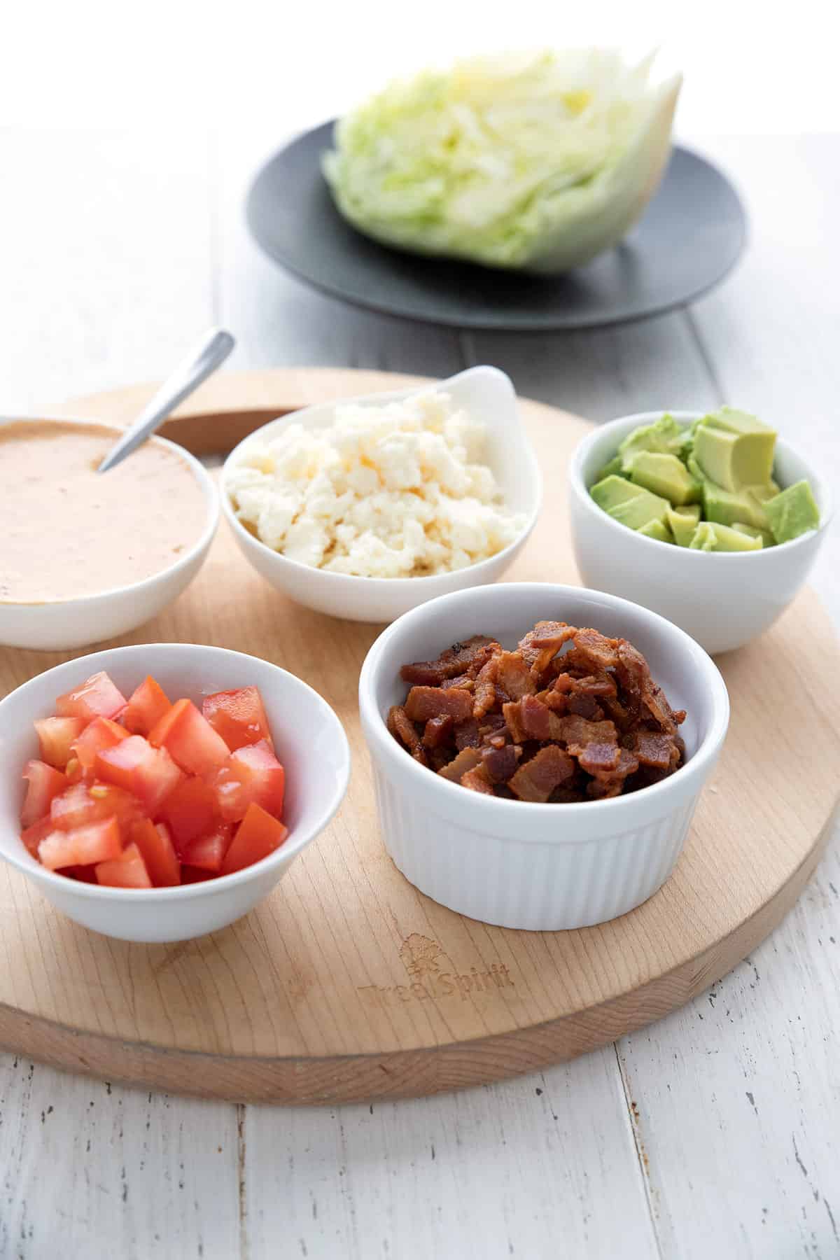 The toppings for Keto Mexican Wedge Salad in white bowls on a cutting board.