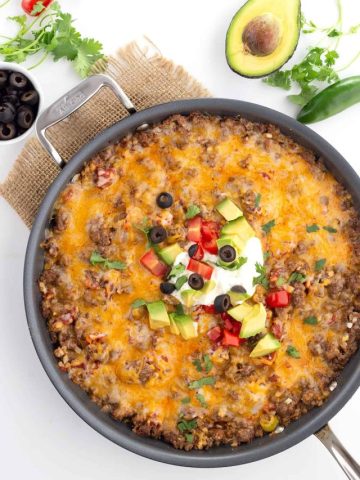 Top down image of Mexican Cauliflower Rice in a large skillet, with avocado, cilantro, jalapeno and olives all around.