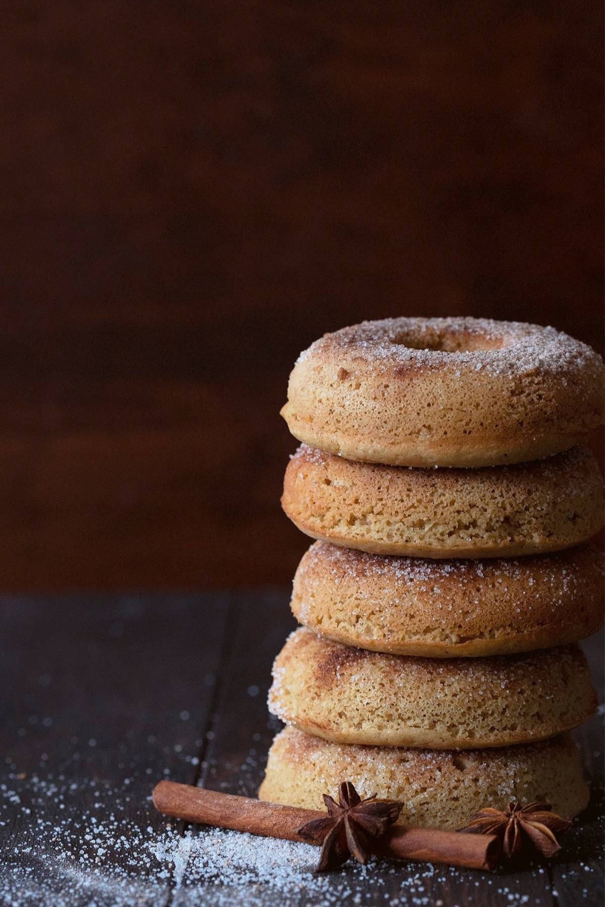 A stack of keto almond flour donuts on a brown wooden table, with cinnamon sticks and star anise around it.