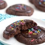 A keto brownie cookie broken open on a white plate with more cookies in the background.