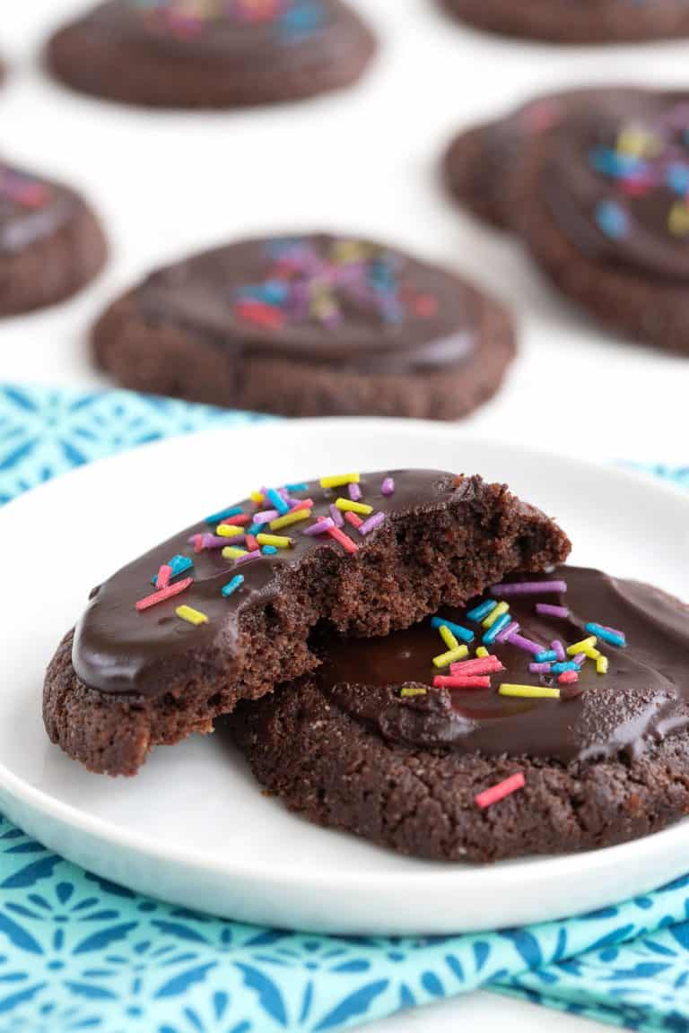 A keto brownie cookie broken open on a white plate with more cookies in the background.