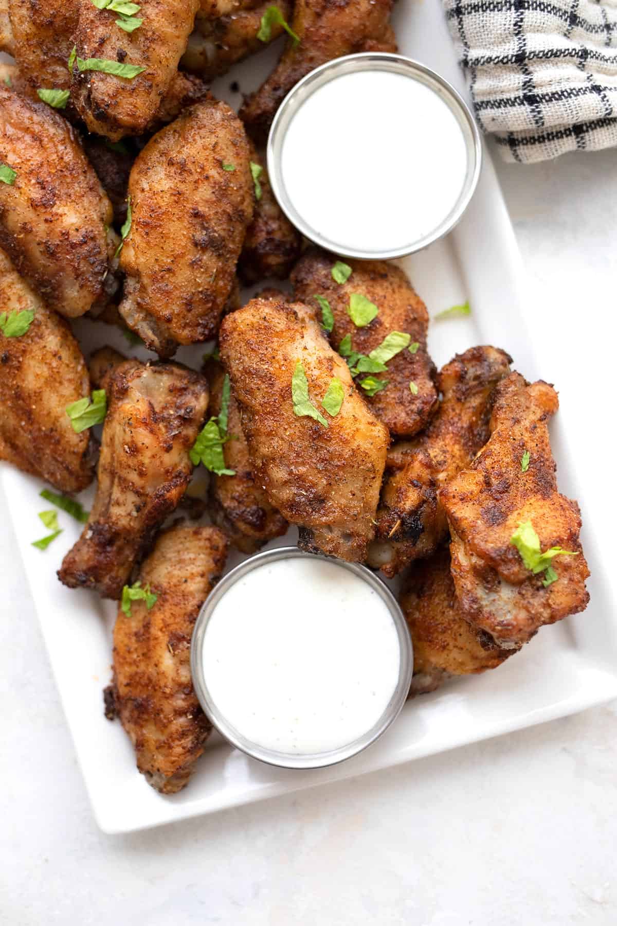 Top down image of Keto Cajun Wings on a white platter with bowls of dipping sauce.