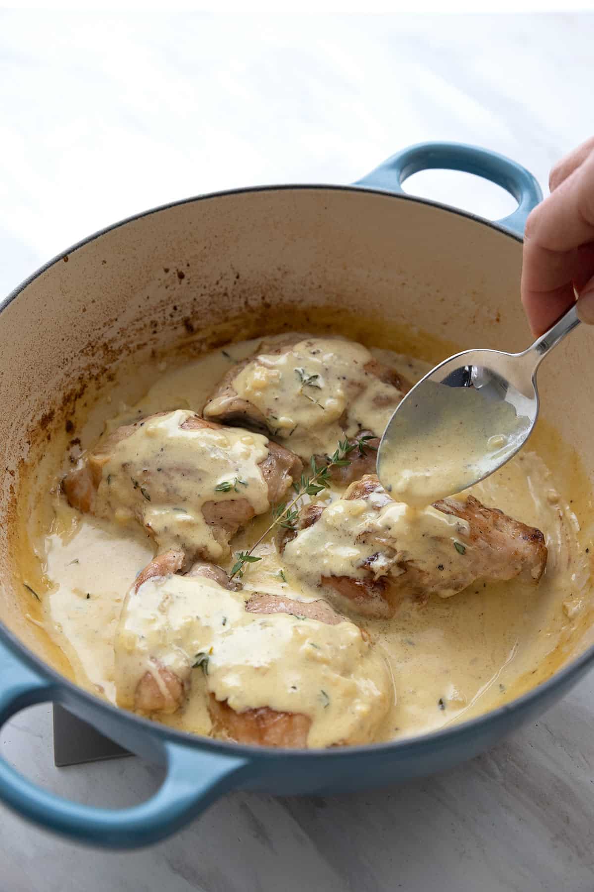 Chicken Dijon in a blue enamelled skillet with a spoon pouring the sauce over.