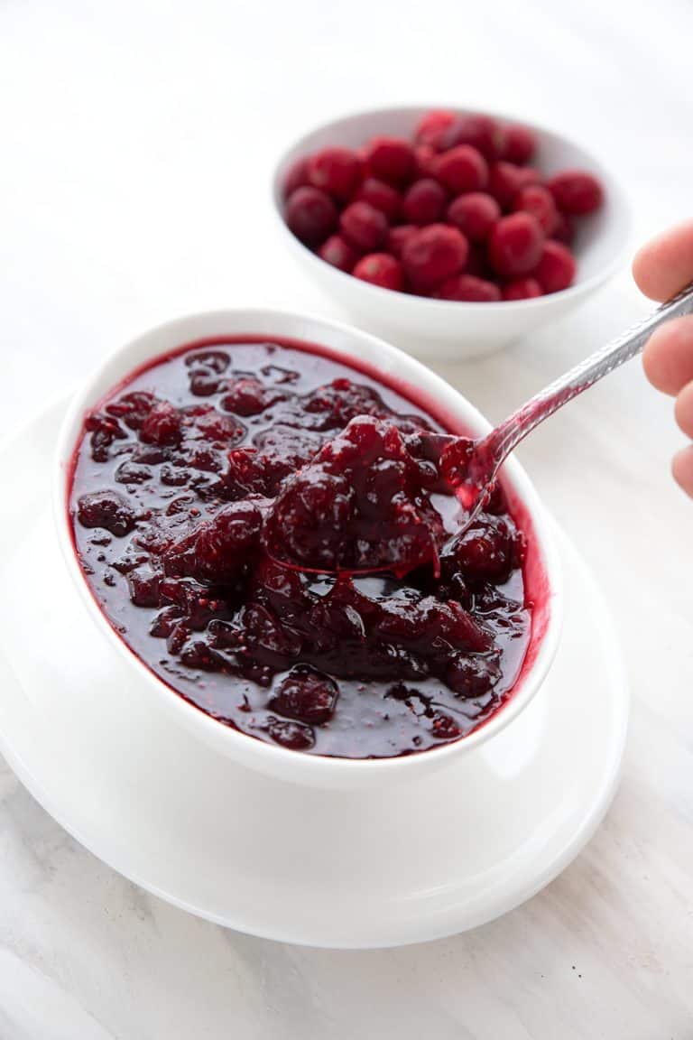 A spoon digging into sugar free cranberry sauce with a bowl of cranberries in the background.