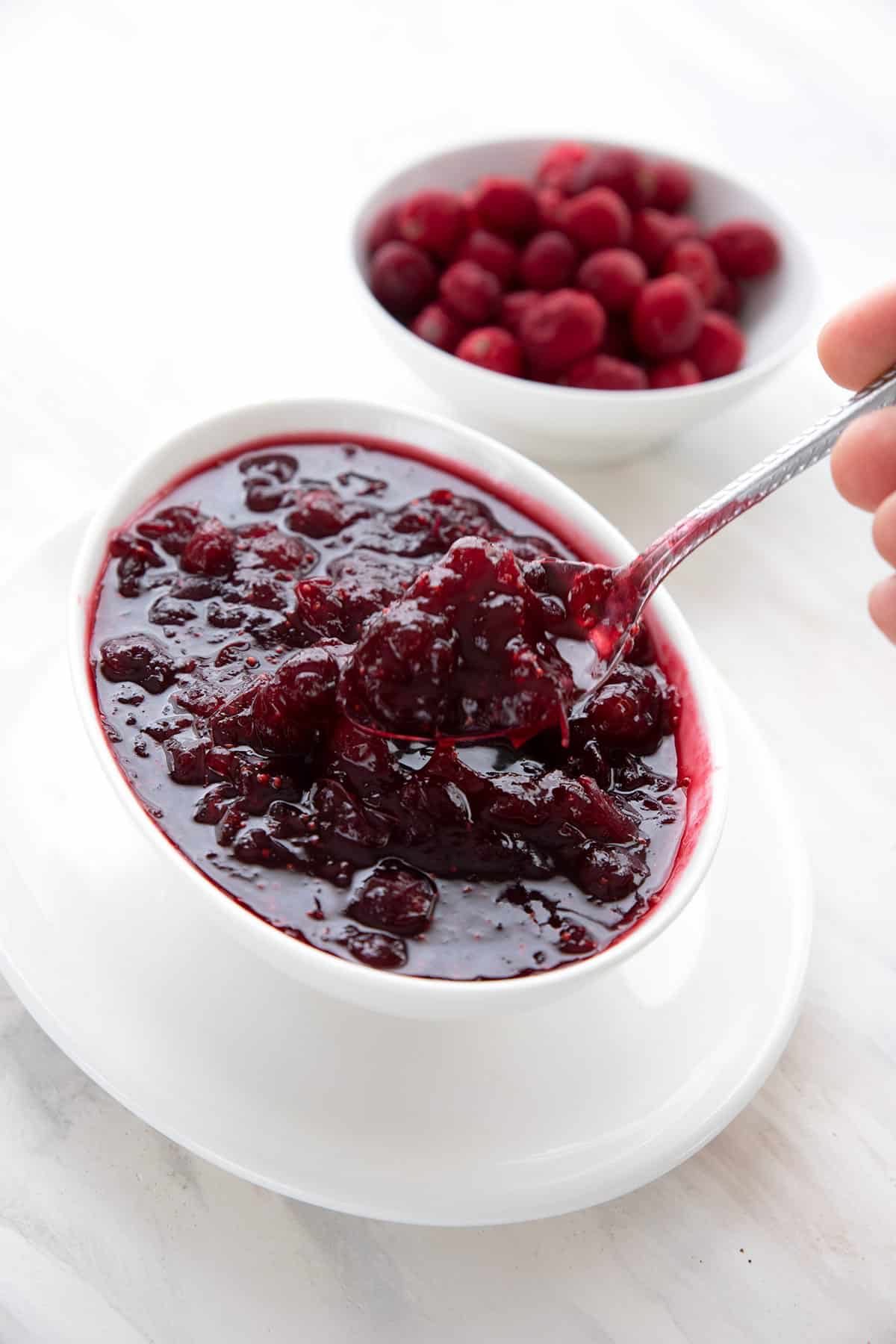 A spoon digging into sugar free cranberry sauce with a bowl of cranberries in the background.