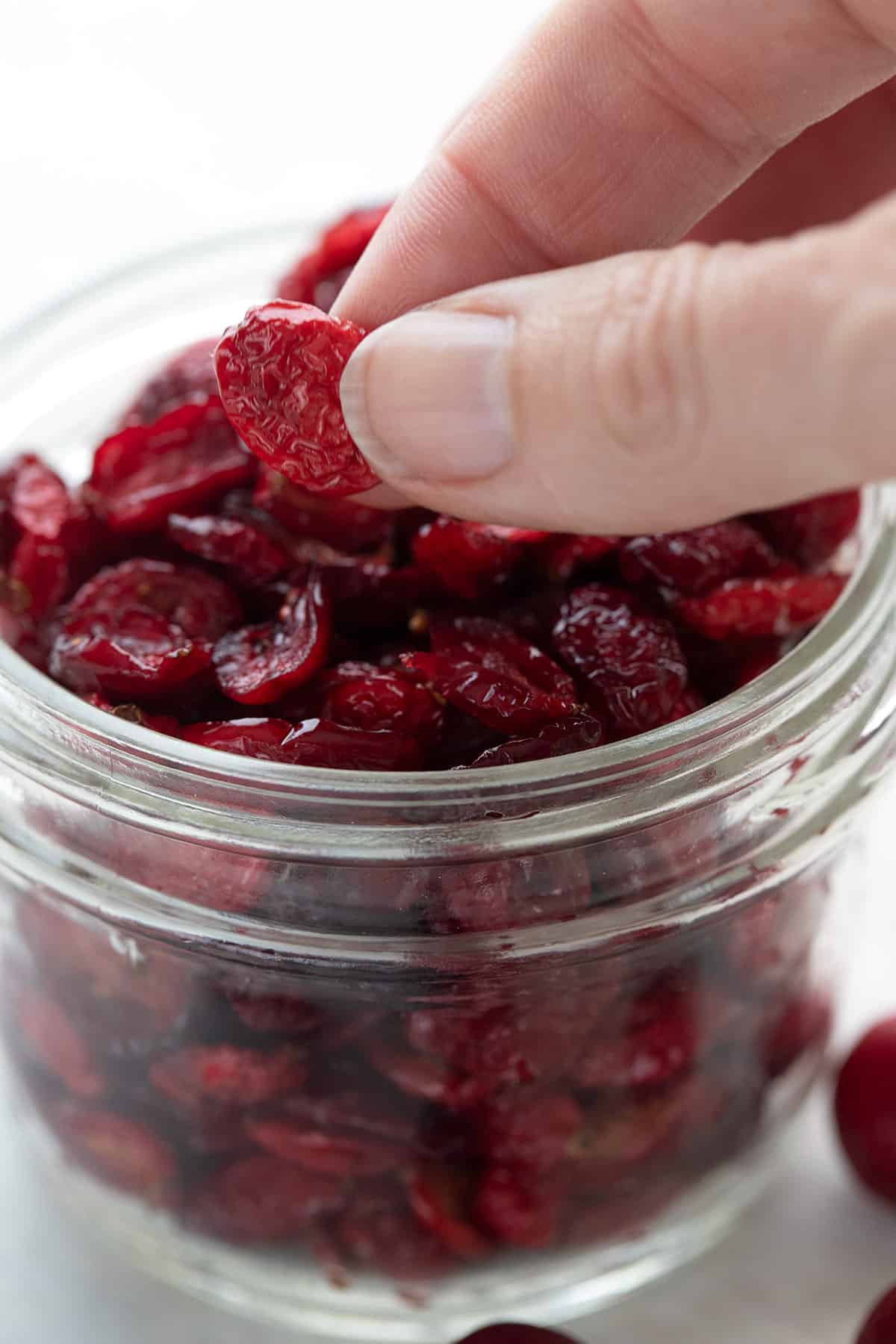 A hand holding up a homemade dried cranberry above the jar.