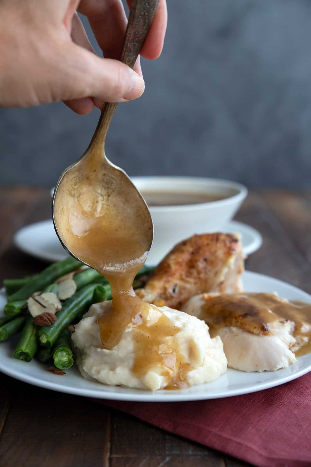 Keto gravy being poured over a plate of turkey, mashed cauliflower, and green beans.
