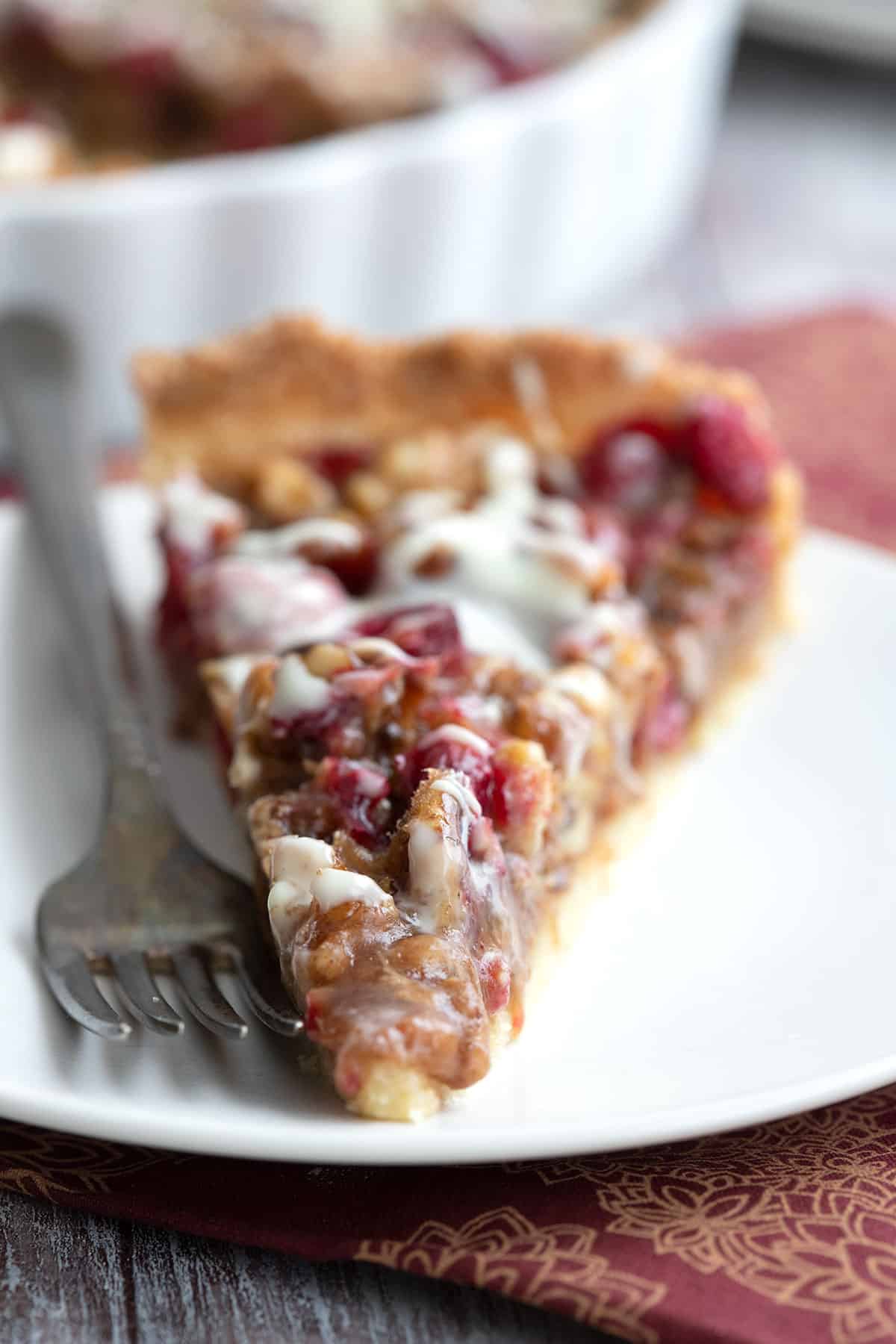 Close up of a slice of Keto Cranberry Walnut Tart on a white plate with a fork.