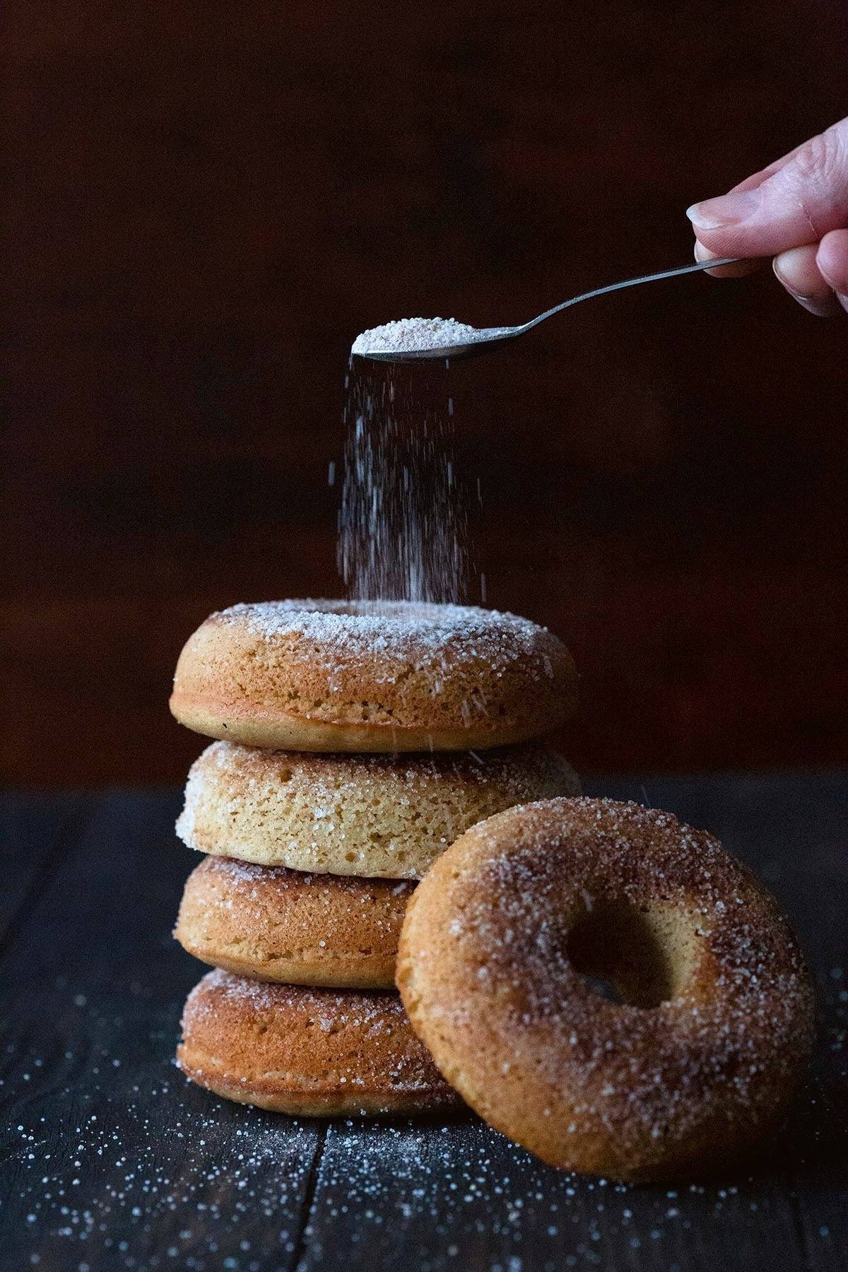 Sprinkling cinnamon and sweetener over keto chai spice donuts.
