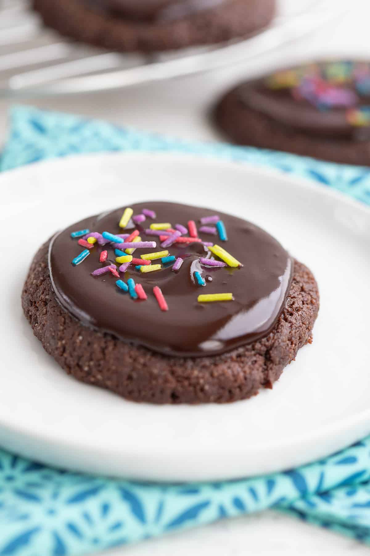 Close up of a keto brownie cookie on a white plate, over a colorful teal napkin.