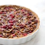 Freshly baked Keto Cranberry Walnut Tart in a white tart pan on a marble counter top.