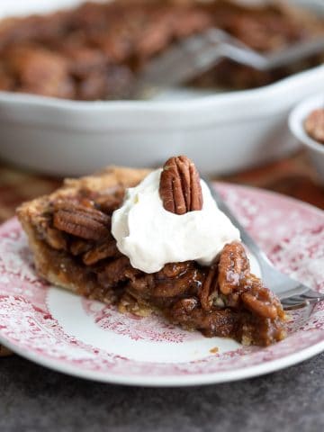 A slice of gooey sugar free pecan pie on a red patterned plate with a fork.