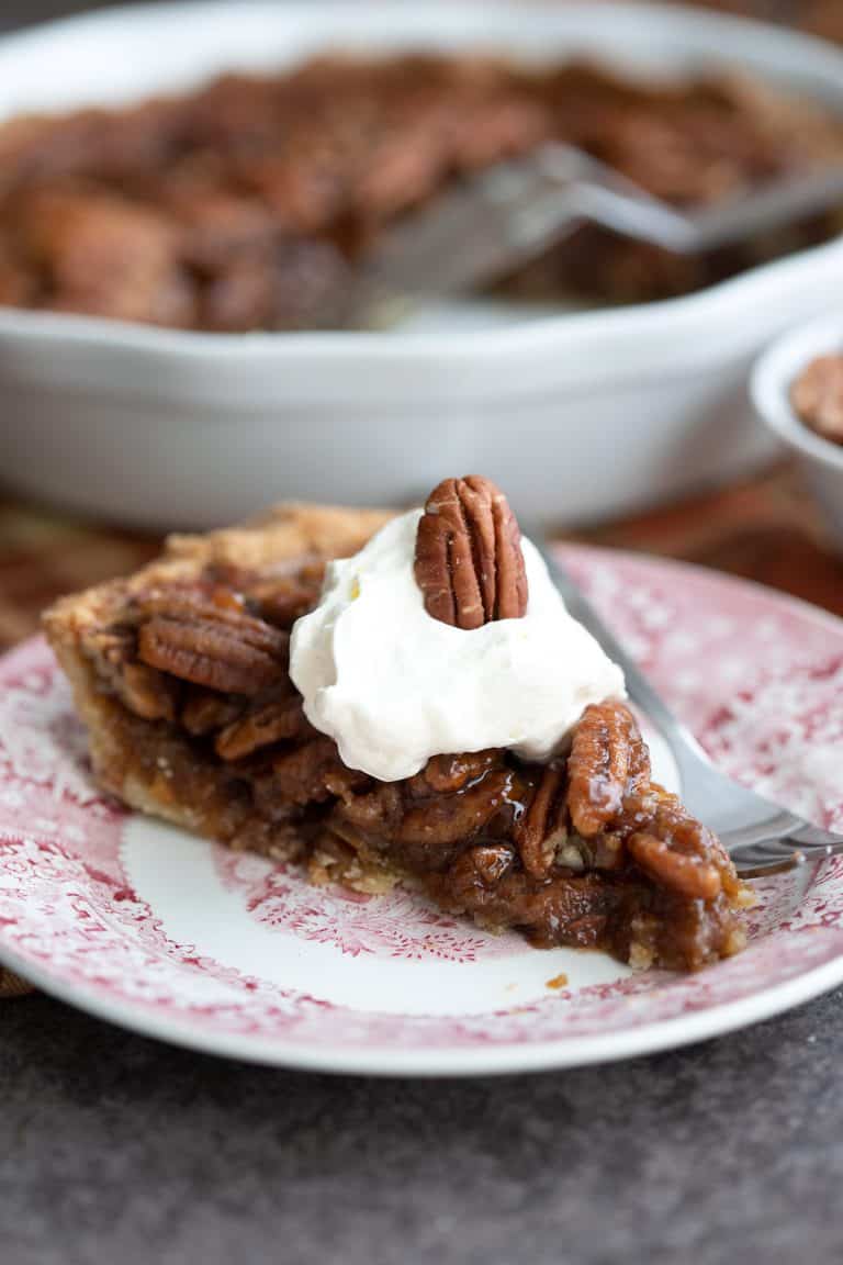 A slice of gooey sugar free pecan pie on a red patterned plate with a fork.