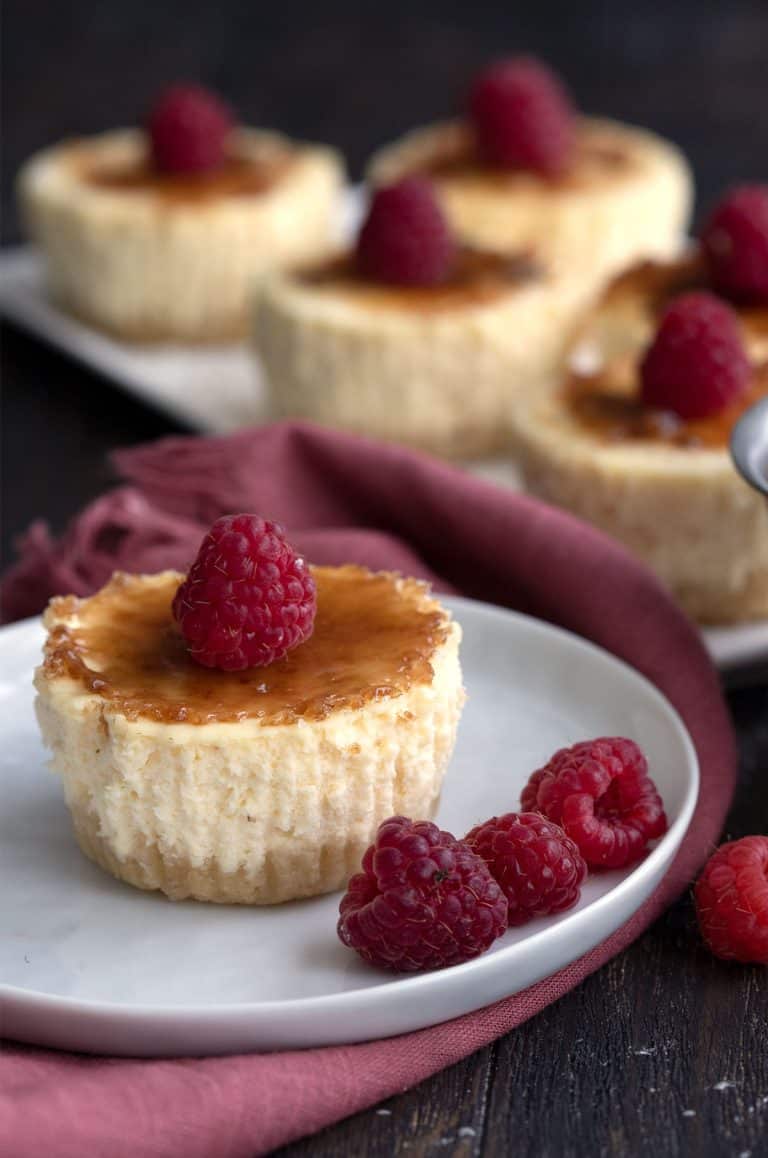 Mini Keto Cheesecake on a white plate with a raspberry on top and a few on the plate.