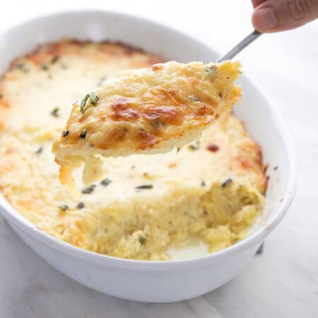 A serving of spaghetti squash casserole being lifted out of a white baking dish on a large spoon.