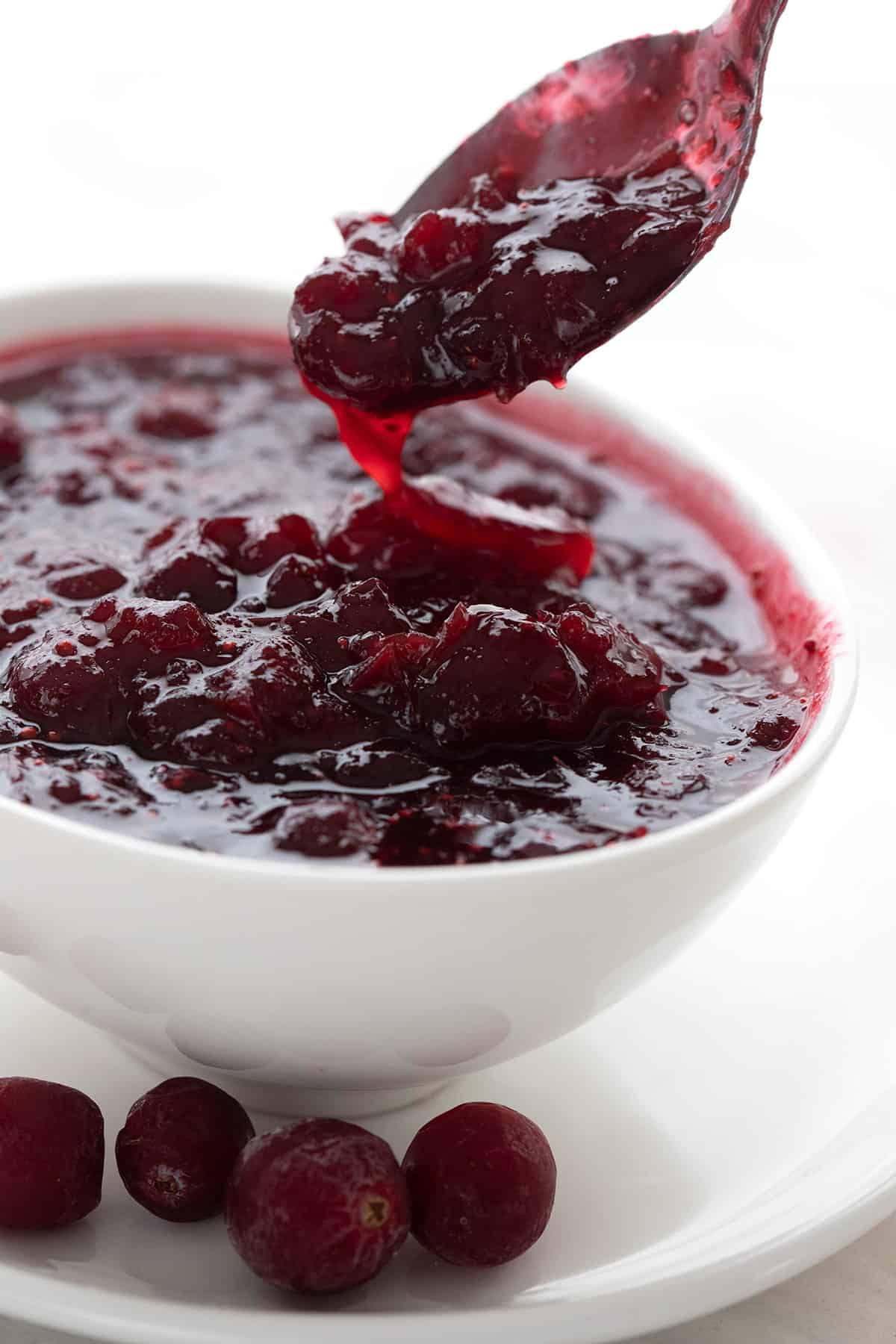 A spoon lifting keto cranberry sauce out of a white bowl.