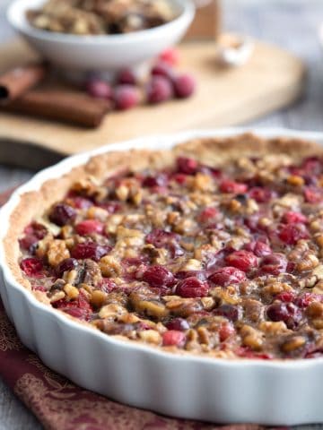 Keto Cranberry Walnut Tart in a white ceramic tart pan with walnuts and cranberries in the background.