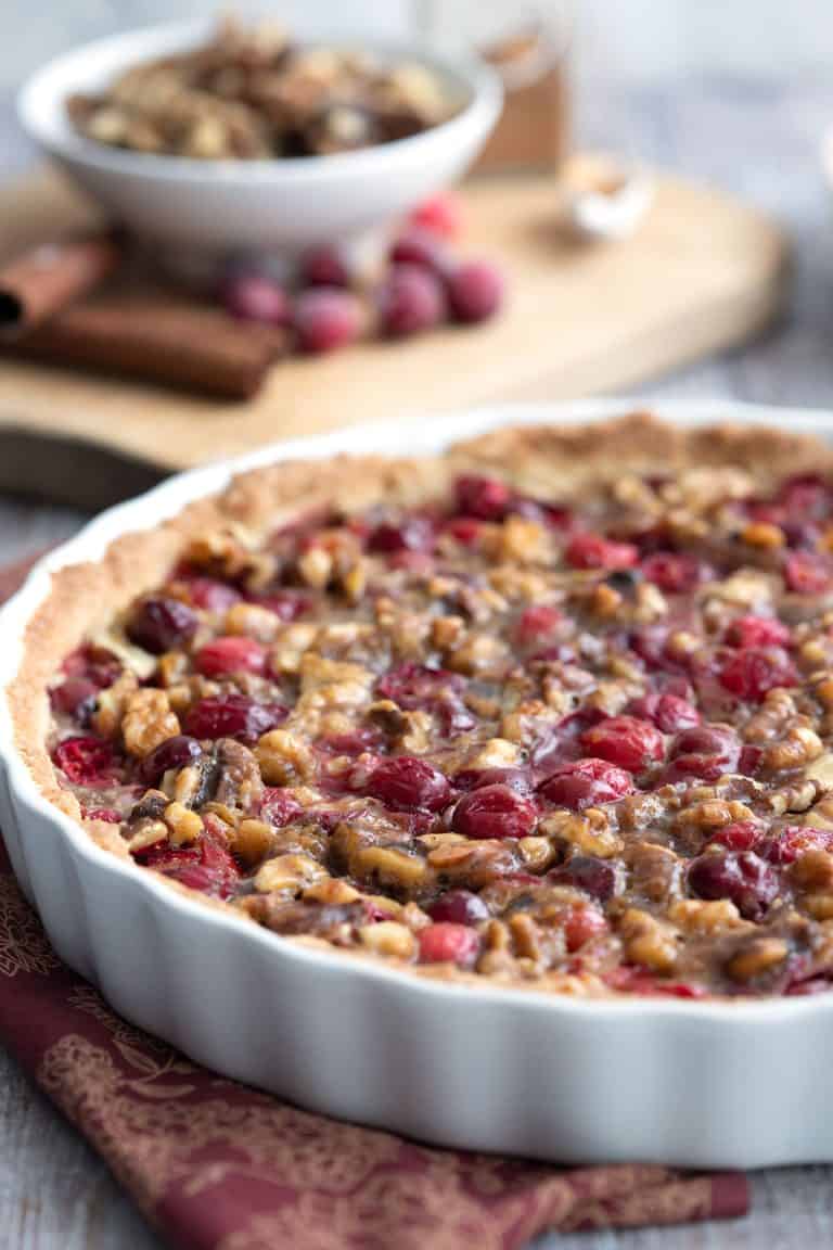 Keto Cranberry Walnut Tart in a white ceramic tart pan with walnuts and cranberries in the background.