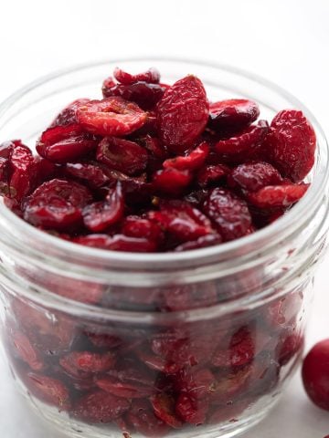 A jar of sugar free dried cranberries with fresh cranberries around it.