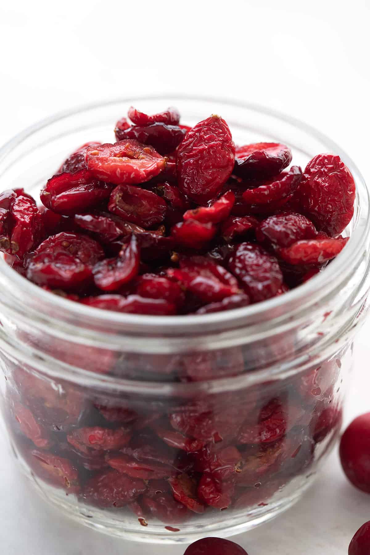 A jar of sugar free dried cranberries with fresh cranberries around it.