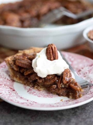 A slice of gooey sugar free pecan pie on a red patterned plate with a fork.