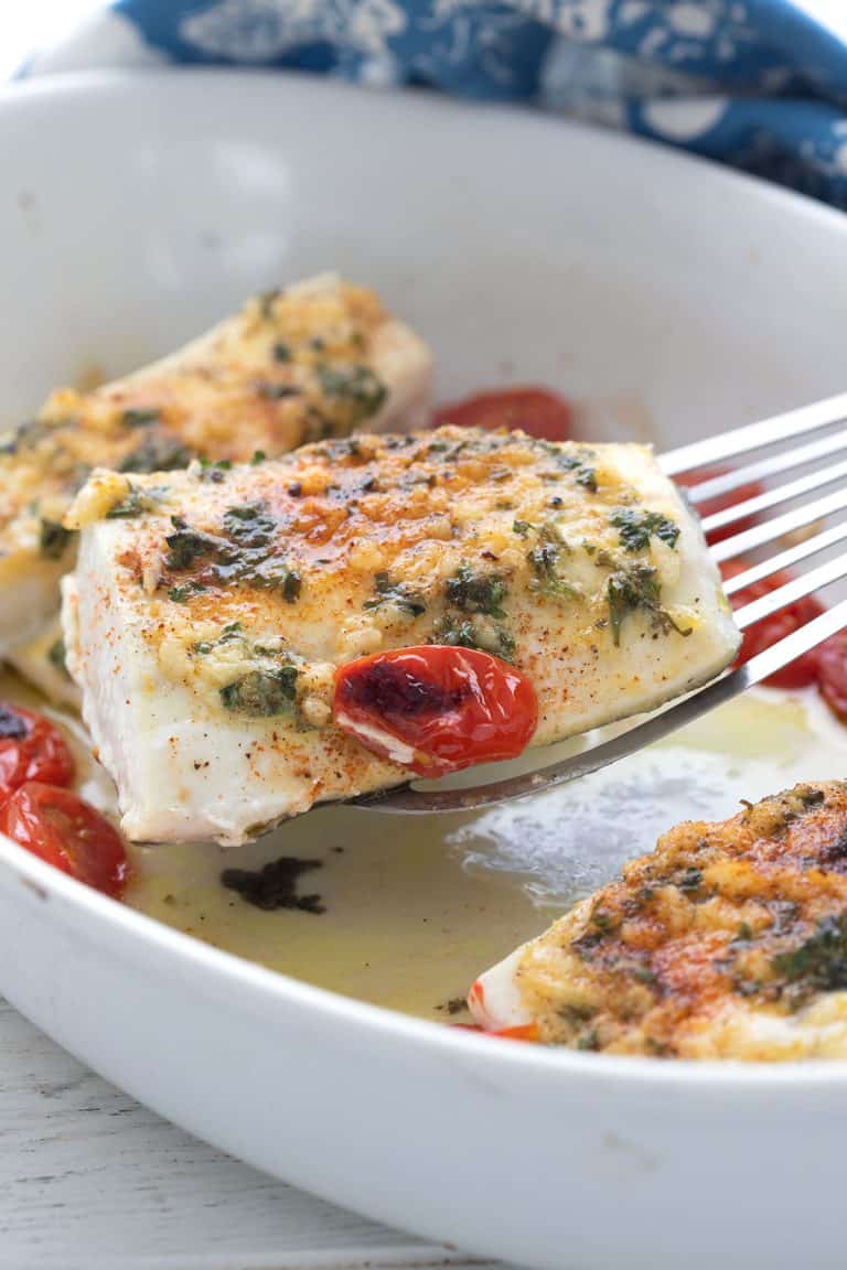 A spatula lifting a piece of baked halibut out of the baking dish.