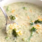 Close up shot of a spoon digging into a bowl of keto broccoli cheese soup.