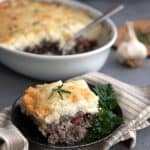 A slice of Keto Shepherd's Pie on a black plate over a striped gray napkin, with the rest of the pie in the background.