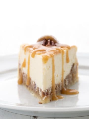 A slice of Keto Pecan Pie Cheesecake on a white plate with keto caramel sauce drizzled over.