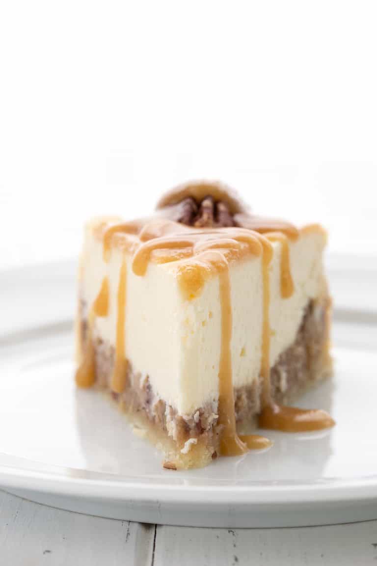 A slice of Keto Pecan Pie Cheesecake on a white plate with keto caramel sauce drizzled over.