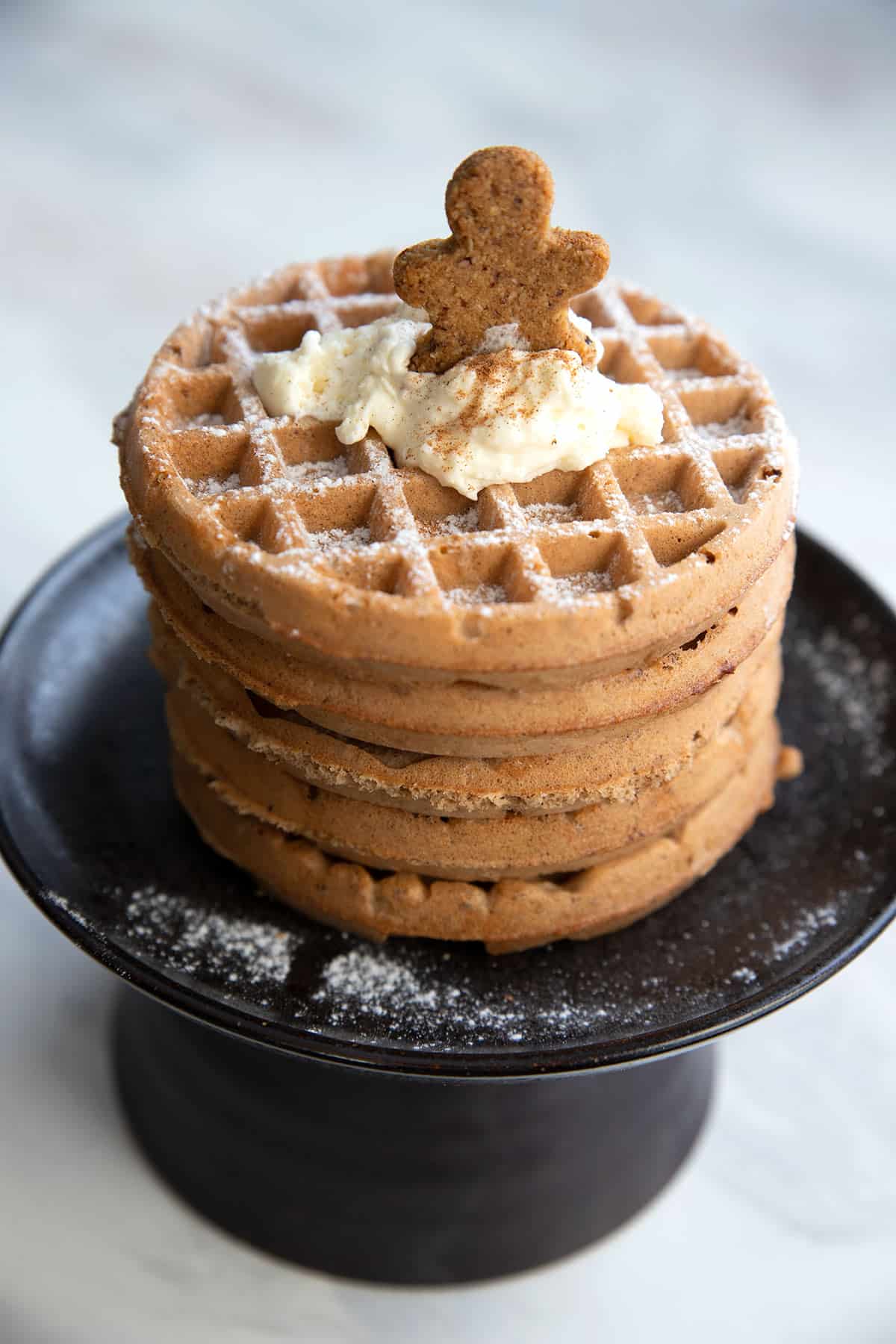A stack of Keto Gingerbread Waffles on a black cake stand.