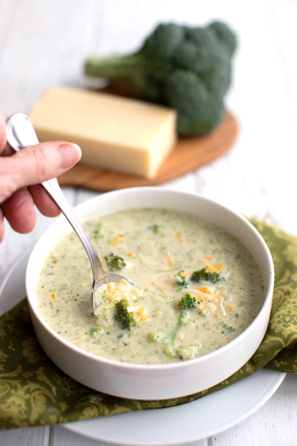 A hand reaching a spoon into a bowl of keto broccoli cheese soup.