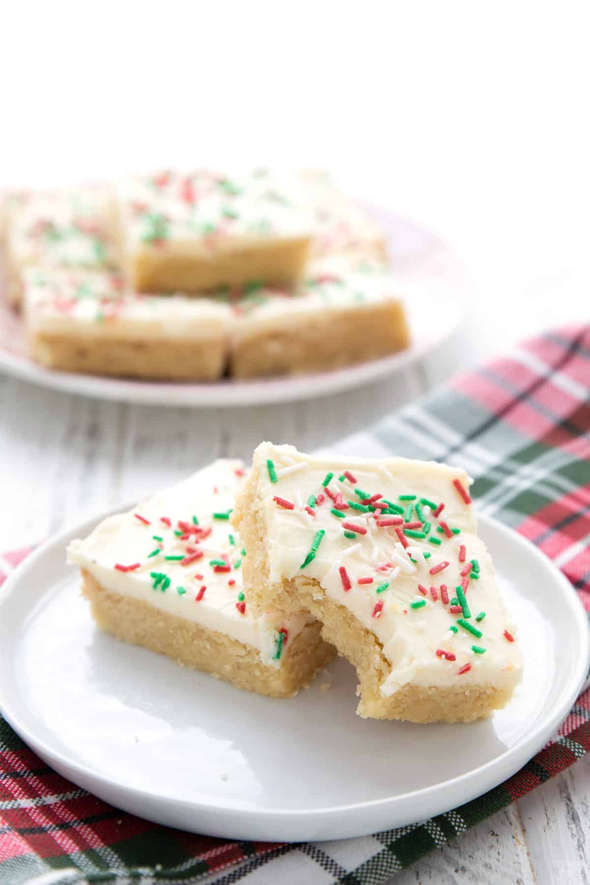 Two holiday sugar cookie bars on a white plate over a green and red plaid napkin.