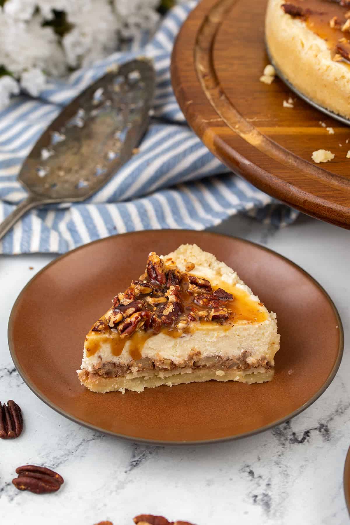 A slice of keto pecan pie cheesecake on a brown plate with a blue striped napkin in the background.