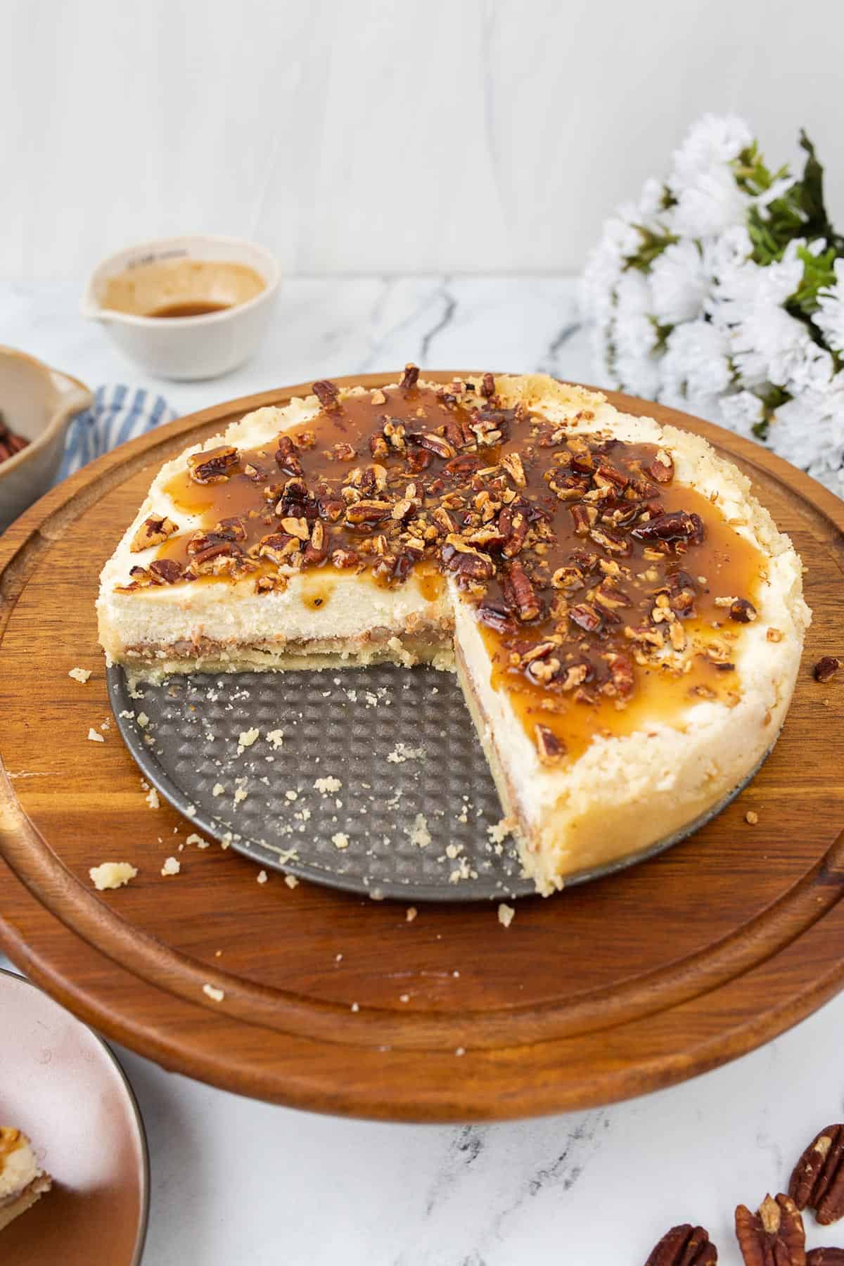 Keto pecan pie cheesecake on a wooden cake stand with several slices cut out.