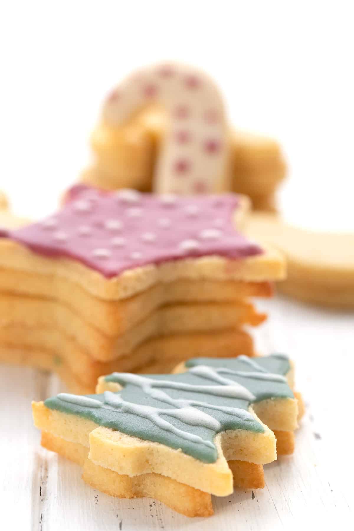 Cut out keto sugar cookies stacked up on a wooden table with the top one decorated like a Christmas tree.
