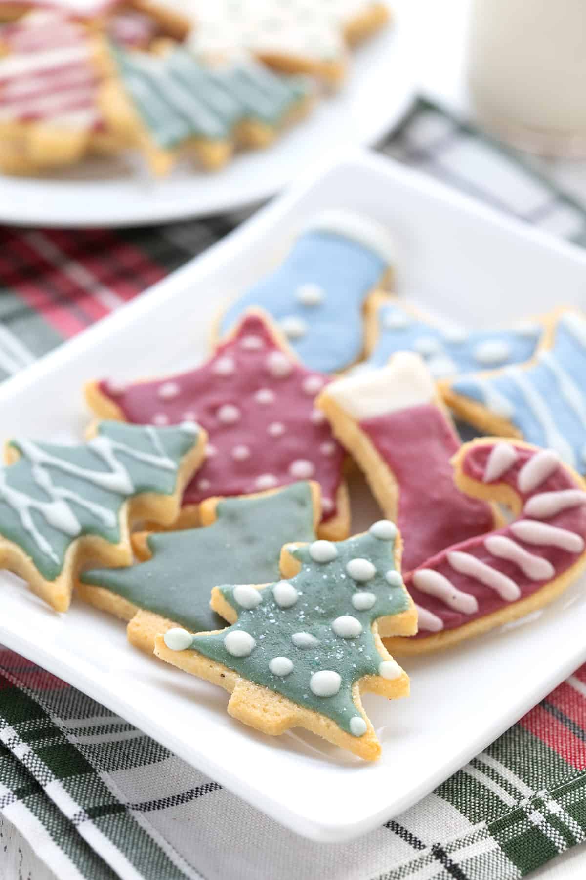 Keto sugar cookies with colorful royal icing on a white plate over a plaid napkin.
