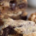 Titled image close up of a keto walnut chocolate chunk blondies on a wooden table.