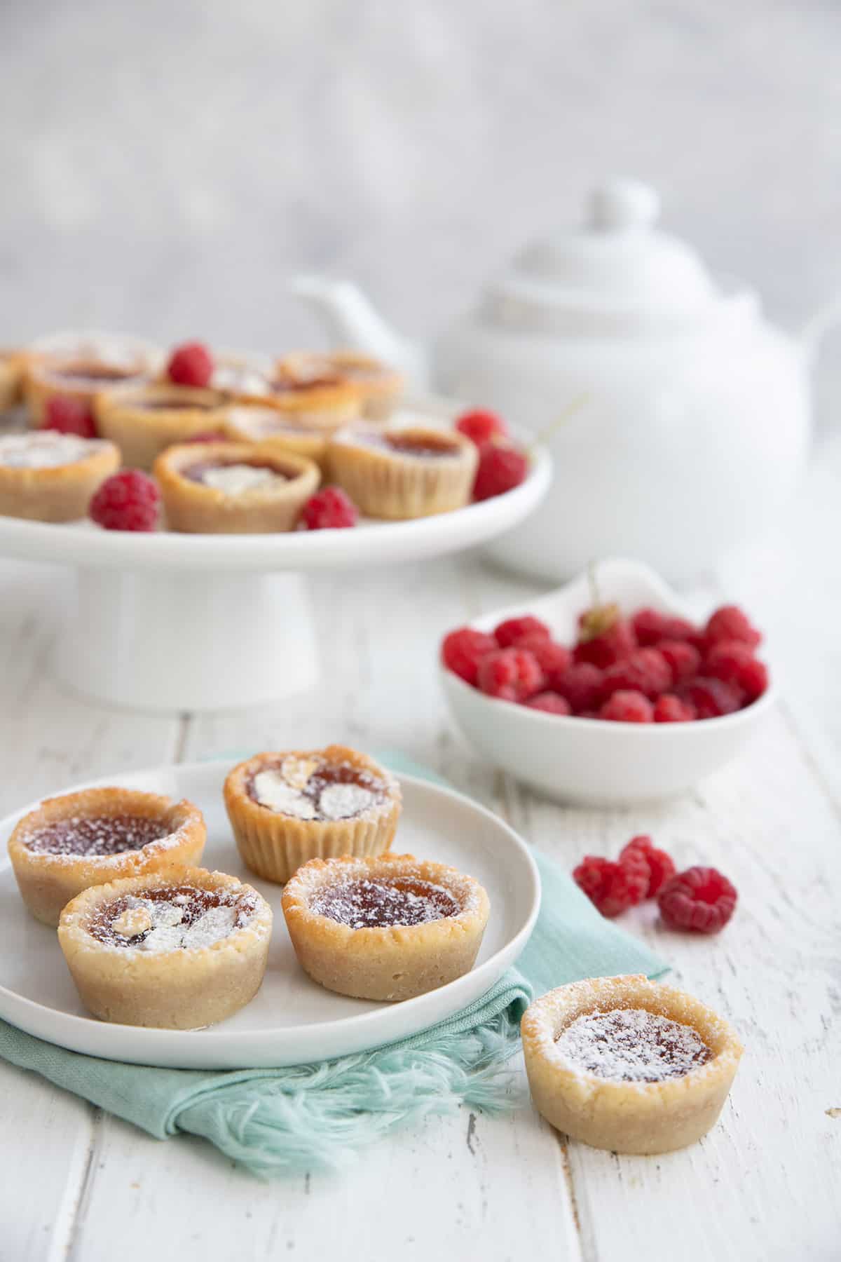 A white table set with a platter of jam tarts and a bowl of raspberries.