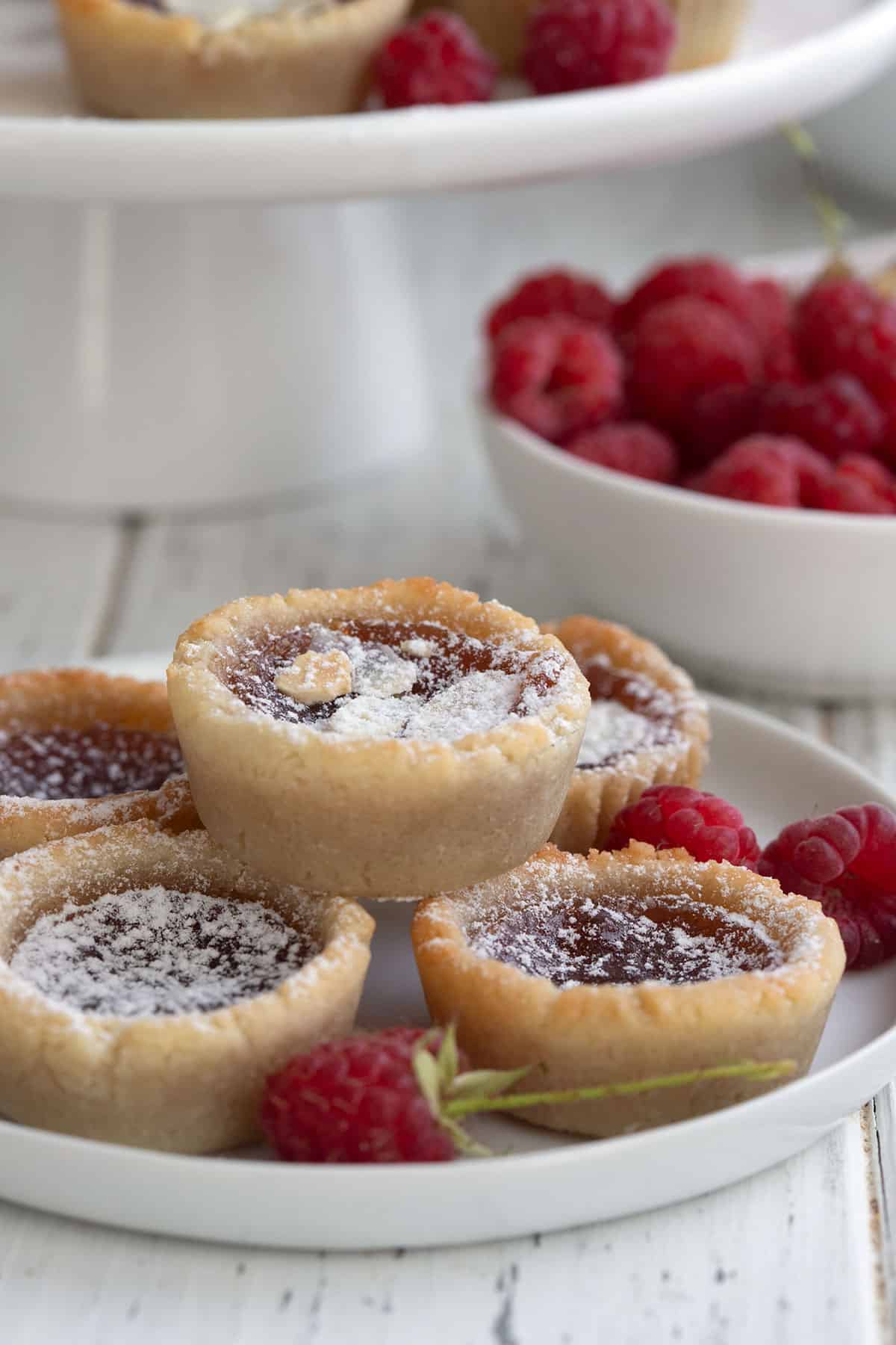 Keto jam tarts on a white plate with raspberries.
