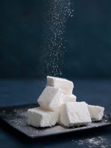 Powdered sweetener being sprinkled over a pile of sugar free marshmallows.