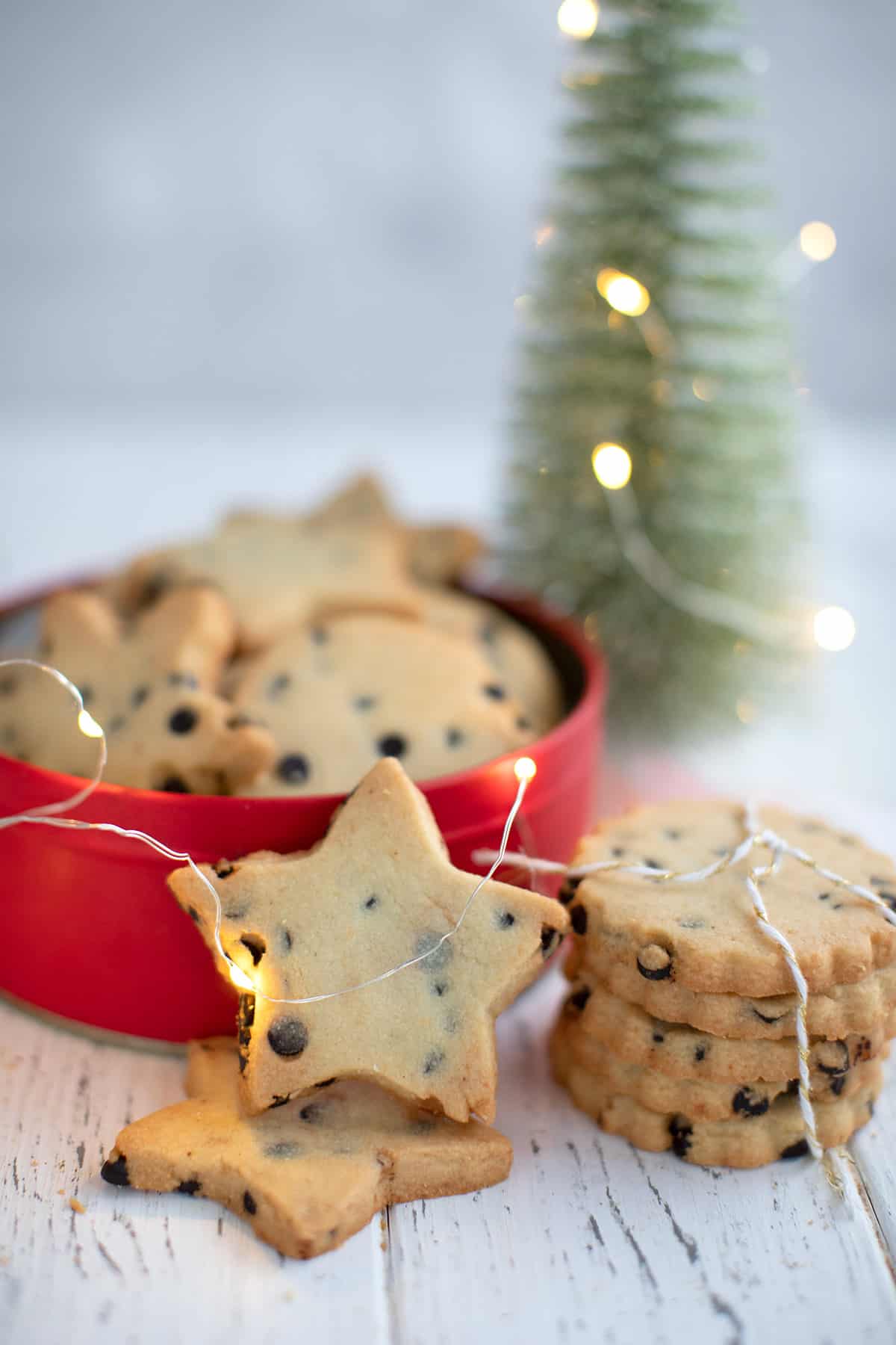 Keto shortbread cookies piled up in front of a cookie tin and surrounded by holiday lights.