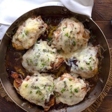 Top down image of French Onion Chicken in a stainless steel skillet on a wooden table.