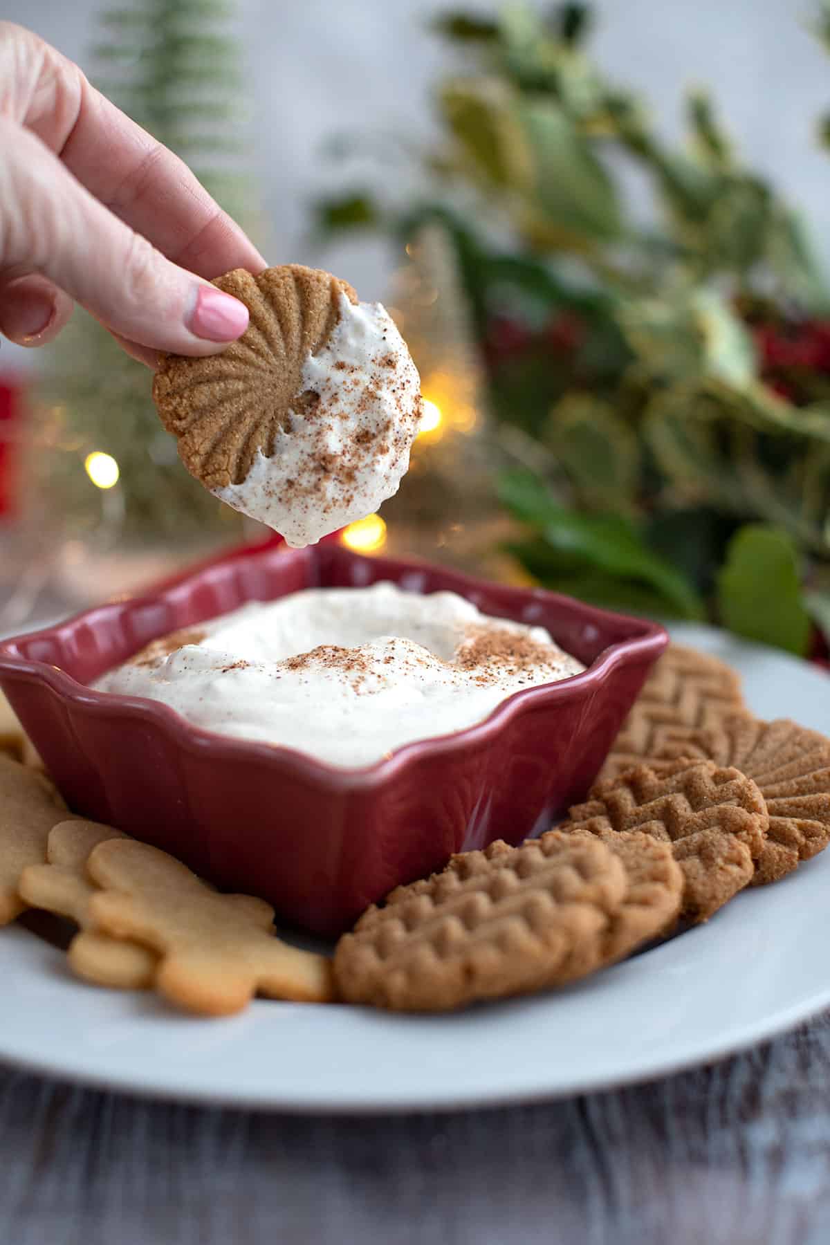 A hand holding a ginger cookie dipped in Keto Eggnog Dip.