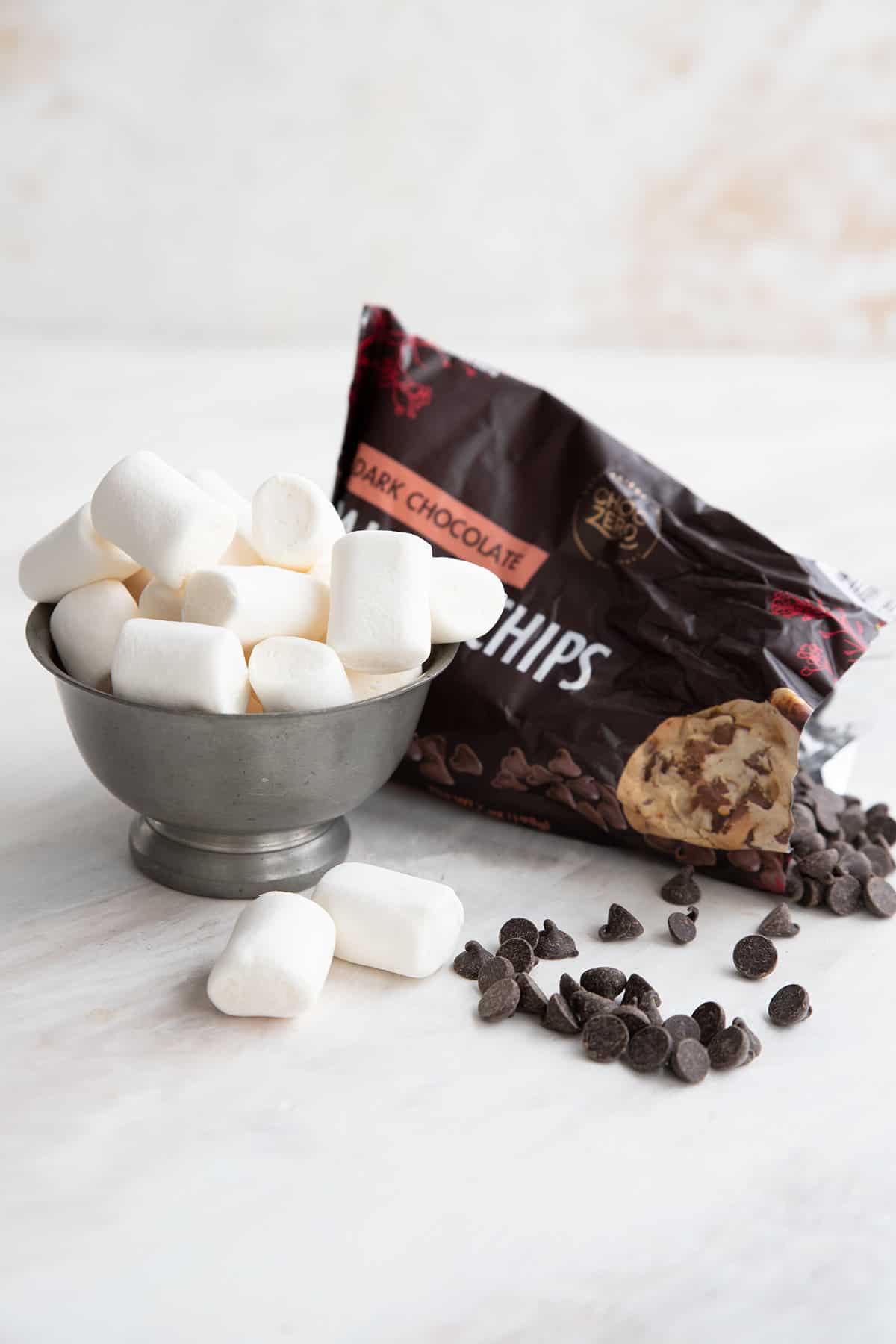 Keto sugar free marshmallows in a bowl beside an open bag of keto chocolate chips.