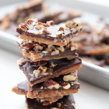 A stack of sugar free toffee in front of a pan with more broken pieces of toffee.