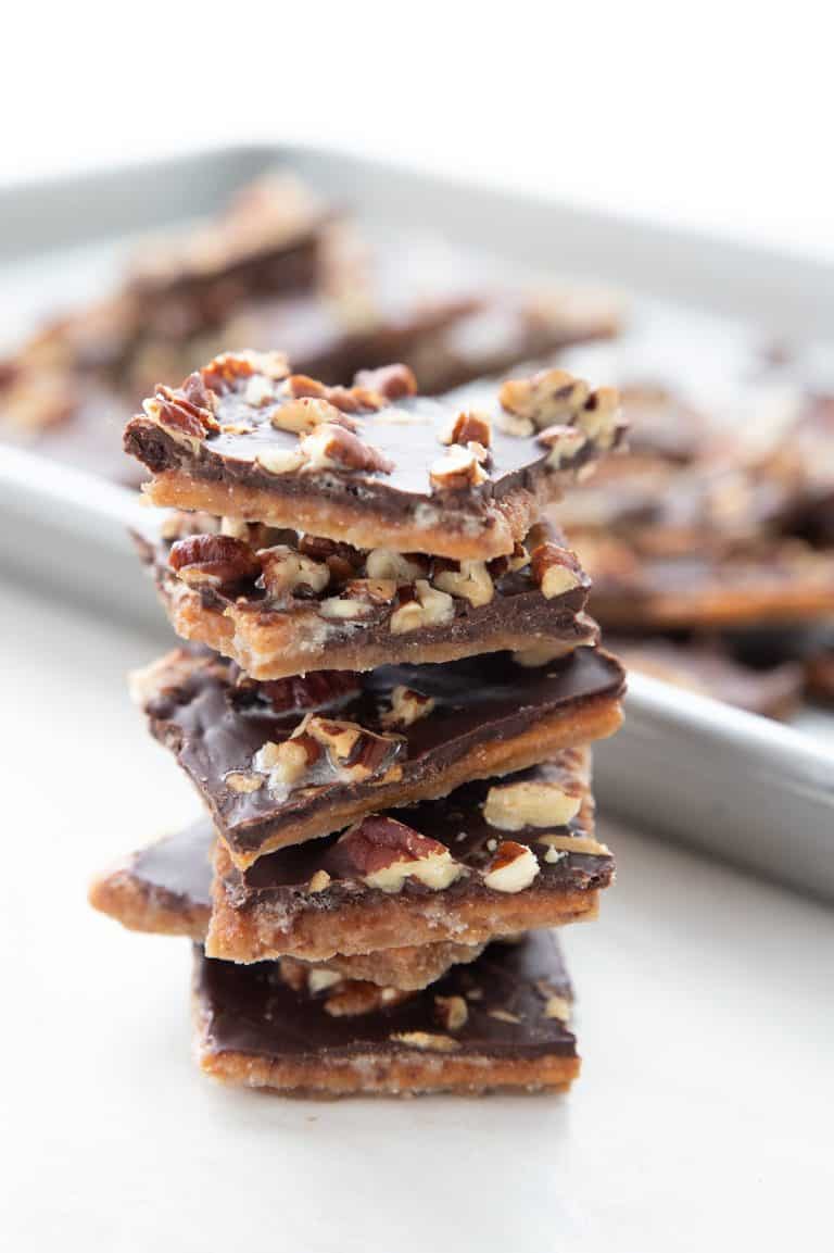 A stack of sugar free toffee in front of a pan with more broken pieces of toffee.